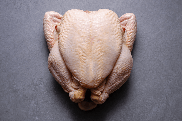 A raw, whole chicken carcass photographed from directly above on a dark gray textured surface.